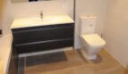 Modernes Badezimmer mit dunklem Waschtischunterschrank, weißem WC und beigen Fliesen in Luxusvilla Marratxí