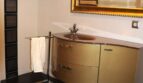 Elegantes Badezimmer mit goldenem Waschtischunterschrank, verziertem Spiegel und dunklen Bodenfliesen in Mallorca-Villa.