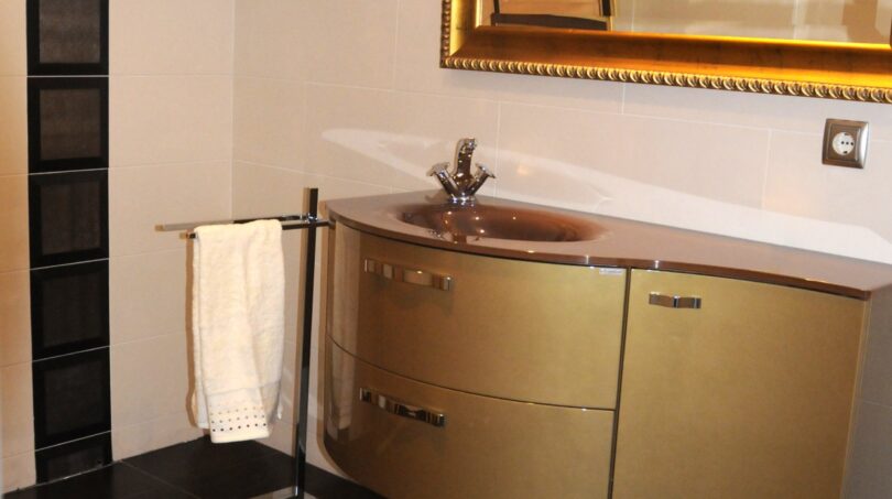 Elegantes Badezimmer mit goldenem Waschtischunterschrank, verziertem Spiegel und dunklen Bodenfliesen in Mallorca-Villa.