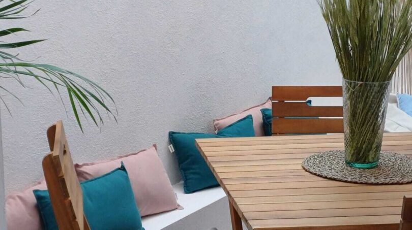Sonnige Terrasse mit Holztisch, Stühlen und Bank mit bunten Kissen in Erdgeschosswohnung Palma de Mallorca