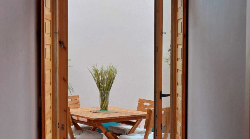 Blick durch geöffnete Holzflügeltür auf überdachte Terrasse mit Holztisch und Stühlen, Erdgeschosswohnung Palma