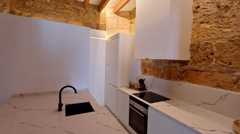 Moderne weiße Küche mit Marmorarbeitsplatte, schwarzem Armatur und Natursteinwand in Erdgeschosswohnung Palma