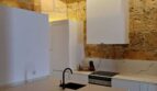 Moderne weiße Küche mit Marmorinsel, schwarzem Wasserhahn und rustikaler Steinwand in Erdgeschosswohnung Palma