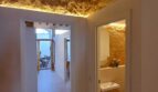Flur mit Natursteinwand, Holzbalken und LED-Beleuchtung, Blick in Bad und Wohnbereich