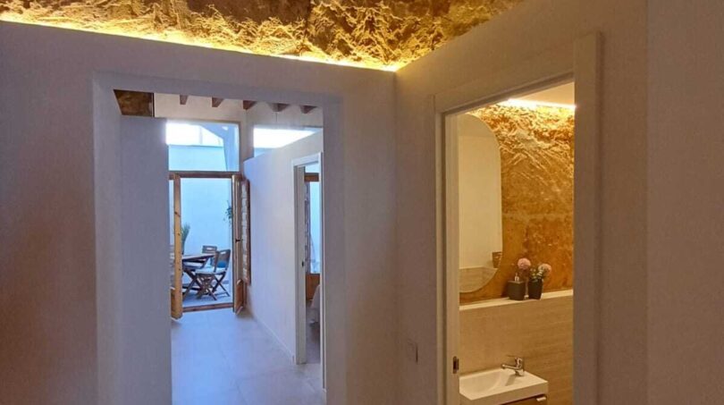Flur mit Natursteinwand, Holzbalken und LED-Beleuchtung, Blick in Bad und Wohnbereich