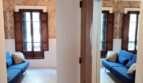 Flur der Erdgeschosswohnung in Palma mit Blick ins Wohnzimmer, blauem Sofa, Natursteinwand und Holzfensterläden