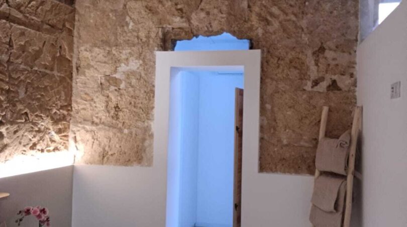 Schlafzimmer mit freiliegender Natursteinwand, Holzbalkendecke und weißer Tür in Erdgeschosswohnung, Palma