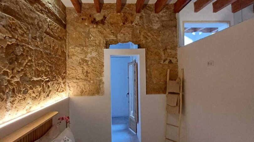 Schlafzimmer mit Natursteinwand, Holzbalkendecke und Blumenbettwäsche in Erdgeschosswohnung Palma