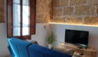 Wohnzimmer mit blauem Sofa, Natursteinwand, Holzbalkendecke und TV in Erdgeschosswohnung in Palma