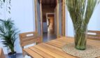 Überdachte Terrasse mit Holztisch und -stühlen, Grünpflanzen und Blick in den Innenbereich der Erdgeschosswohnung in Palma