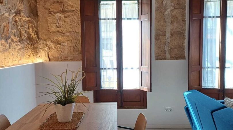 Wohnzimmer mit Natursteinwand, Holzbalkendecke, blauem Sofa und Esstisch in Erdgeschosswohnung, Palma de Mallorca