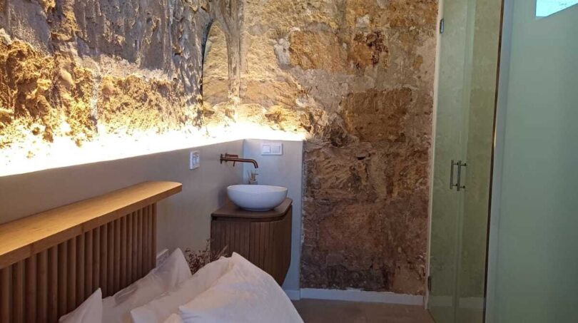 Schlafzimmer mit Natursteinwand, Holzbalkendecke, Doppelbett und integriertem Waschbecken in Palma