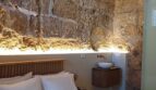 Schlafzimmer mit Doppelbett, rustikaler Steinwand, Holzbalkendecke und elegantem Waschtisch in Palma de Mallorca