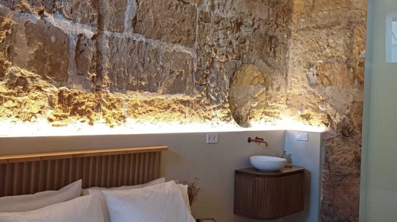 Schlafzimmer mit Doppelbett, rustikaler Steinwand, Holzbalkendecke und elegantem Waschtisch in Palma de Mallorca
