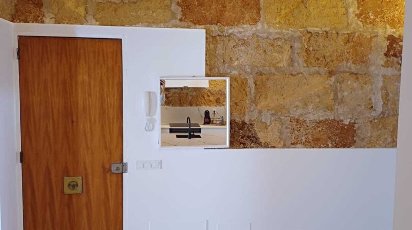 Küche mit rustikaler Natursteinwand, Holzbalkendecke, weißer Marmorarbeitsplatte und Holztür in Palma