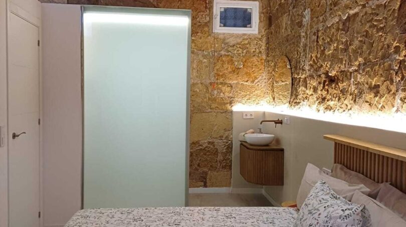 Schlafzimmer mit Doppelbett, Natursteinwand, Holzbalkendecke und integriertem Waschbereich in Palma