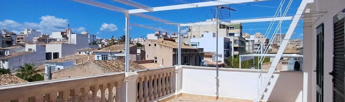 Sonnige Dachterrasse mit Sandsteinboden, Balustrade und Pergola, Blick auf Palmas Altstadt unter blauem Himmel