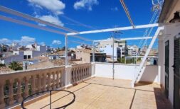 Sonnige Dachterrasse mit Sandsteinboden, Balustrade und Pergola, Blick auf Palmas Altstadt unter blauem Himmel
