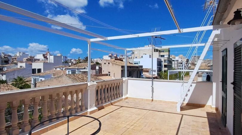 Sonnige Dachterrasse mit Sandsteinboden, Balustrade und Pergola, Blick auf Palmas Altstadt unter blauem Himmel