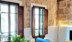 Wohnzimmer mit Natursteinwand, Holzbalkendecke, blauem Sofa und Tulpenstrauß in Erdgeschosswohnung Palma