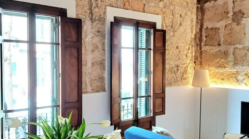 Wohnzimmer mit Natursteinwand, Holzbalkendecke, blauem Sofa und Tulpenstrauß in Erdgeschosswohnung Palma