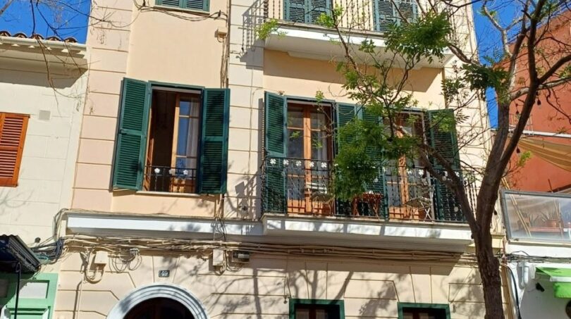Außenansicht eines gepflegten Altbaus in Palma mit grünen Fensterläden, Balkonen und elegantem Rundbogeneingang.