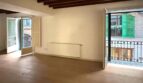 Leerer Wohnraum mit Holzbalkendecke, Betonboden und zwei Balkontüren in renovierter Palma-Wohnung