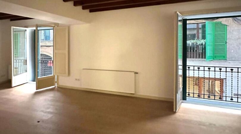 Leerer Wohnraum mit Holzbalkendecke, Betonboden und zwei Balkontüren in renovierter Palma-Wohnung