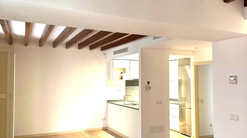 Helles Wohnzimmer mit Holzbalkendecke und offener Küche in renovierter Wohnung in Palma de Mallorca