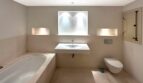 Modernes Badezimmer mit Einbaubadewanne, Wandwaschbecken, WC und eleganter Nischenbeleuchtung in Beige