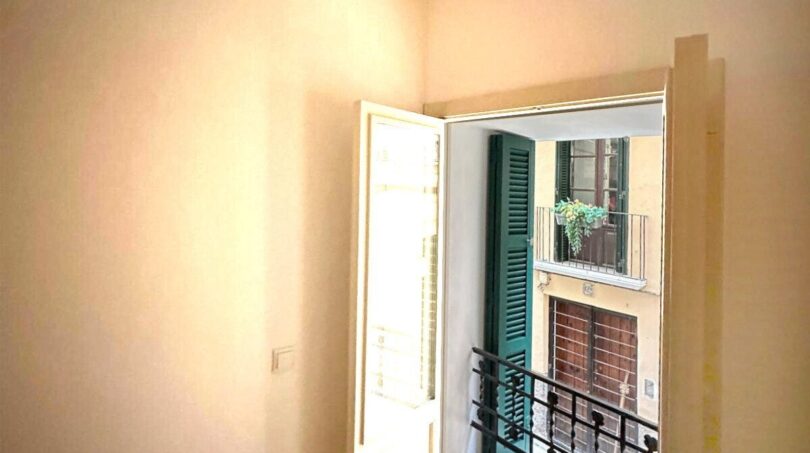 Helles Zimmer mit Balkon und Blick auf mediterrane Altbaufassade mit grünen Fensterläden in Palma