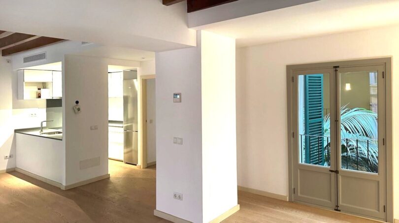 Renoviertes Wohnzimmer mit Holzbalkendecke, offenem Küchenbereich und Balkontür in Palma de Mallorca