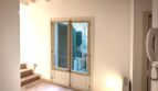 Heller Flur mit Holzdielen, Holzbalkendecke und französischer Tür mit Blick auf grüne Außenjalousien, renovierte Wohnung Palma