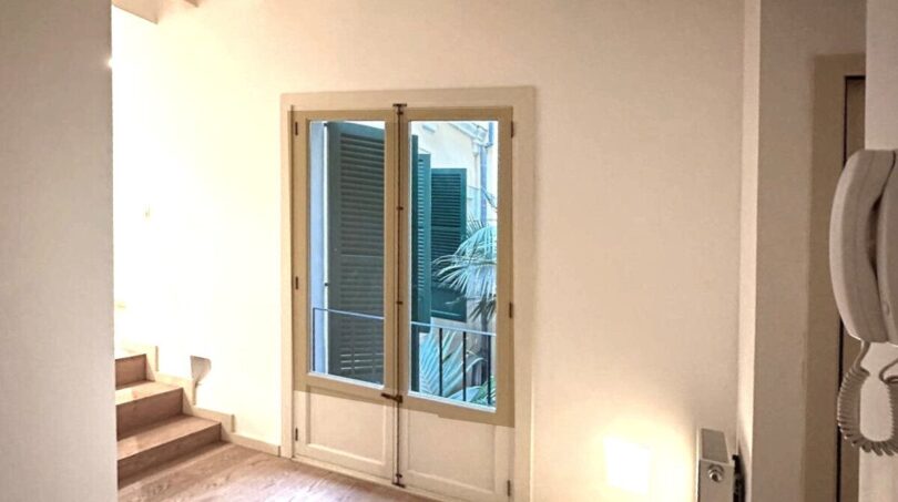 Heller Flur mit Holzdielen, Holzbalkendecke und französischer Tür mit Blick auf grüne Außenjalousien, renovierte Wohnung Palma