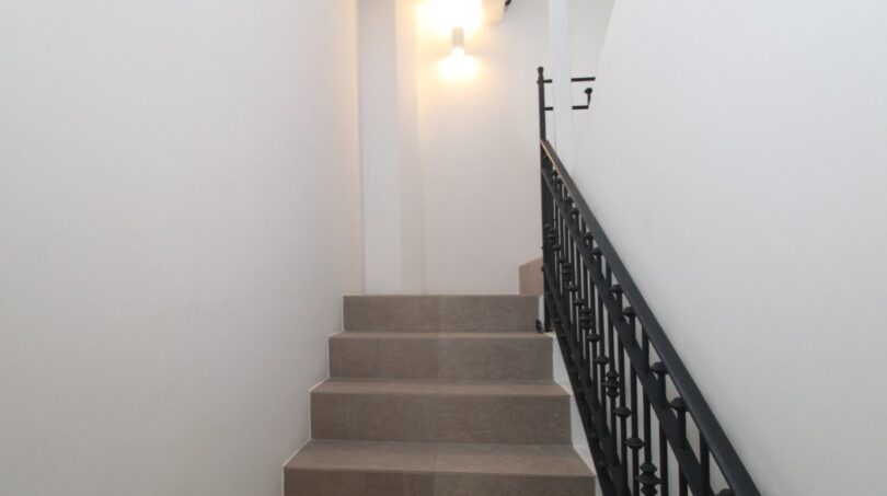 Escalera elegante con escalones de piedra natural, barandilla de hierro forjado e iluminación de pared en el ático Paseo del Borne