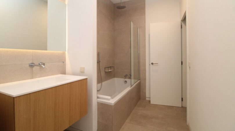 Baño moderno con bañera empotrada, ducha de lluvia y elegante tocador de madera en el ático Paseo del Borne