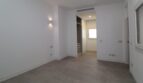 Dormitorio luminoso y vacío con piso de baldosas, aplique de pared y vista del vestidor incorporado en el ático Palma