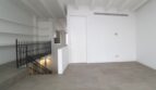 Planta superior luminosa del ático maisonette con escalera de hierro forjado, piso de hormigón y vigas de techo blancas