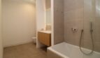 Baño moderno con bañera, tocador de madera, espejo iluminado y baldosas beige en el ático Palma