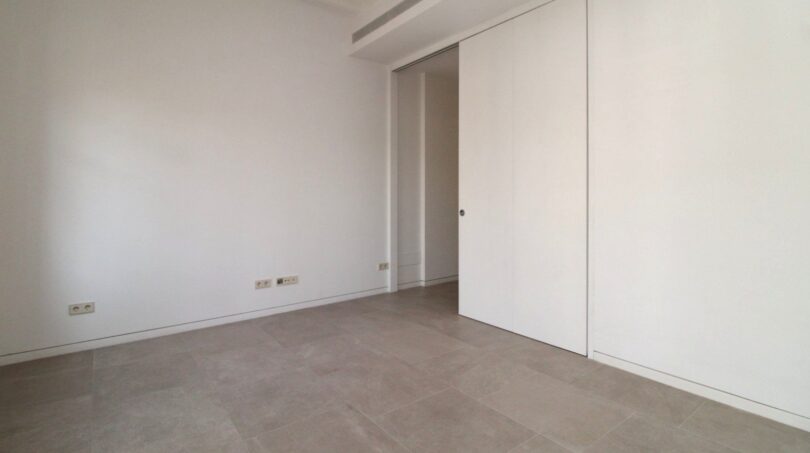 Dormitorio vacío con piso de baldosas gris, paredes blancas y puerta corrediza elegante en el ático Paseo del Borne