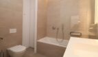 Baño moderno con bañera, mampara de vidrio, inodoro suspendido y baldosas beige en el ático Palma