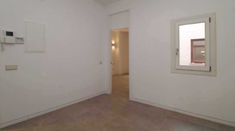 Sala luminosa y vacía con pisos de baldosas, paso al pasillo y pequeña ventana en el ático Born Palma