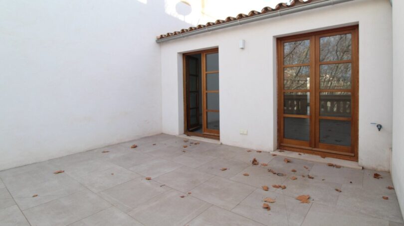 Patio interior luminoso con baldosas de terracota, puertas y ventanas de madera y arquitectura de carácter mediterráneo en el ático Palma.
