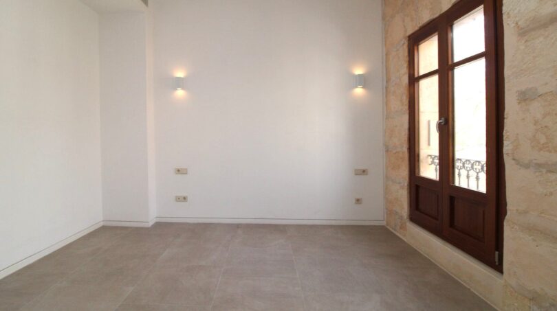 Espacio de estar vacío con apliques de pared, pared de piedra natural y ventanas de madera en el ático maisonette, Paseo del Borne, Palma