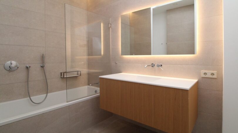 Baño moderno con bañera, tocador de madera flotante y espejo iluminado en el ático Palma