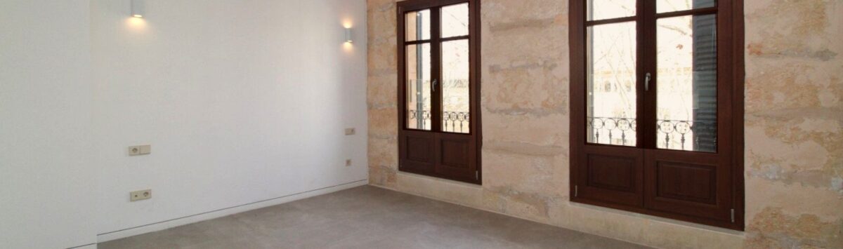 Sala de estar luminosa con pared de piedra natural, dos ventanas de madera y suelo de baldosas moderno en el ático Paseo del Borne