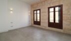Sala de estar luminosa con pared de piedra natural, dos ventanas de madera y suelo de baldosas moderno en el ático Paseo del Borne