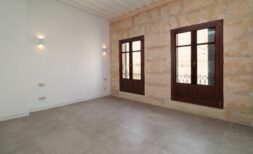 Helles Wohnzimmer mit Natursteinwand, zwei Holzfenstern und modernem Fliesenboden im Penthouse Paseo del Borne