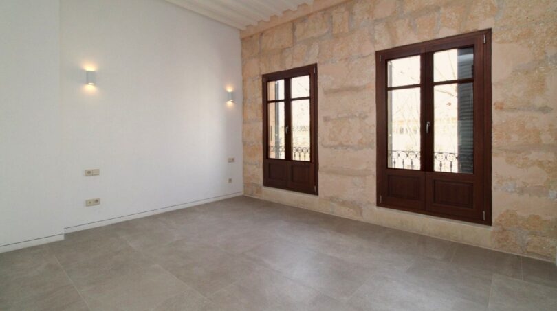 Sala de estar luminosa con pared de piedra natural, dos ventanas de madera y suelo de baldosas moderno en el ático Paseo del Borne