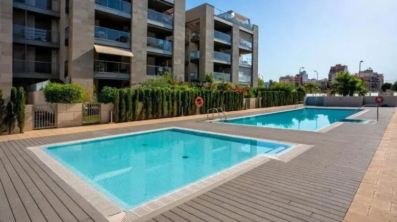 Piscina comunitaria con terraza de madera y complejo de apartamentos moderno en Palma de Mallorca